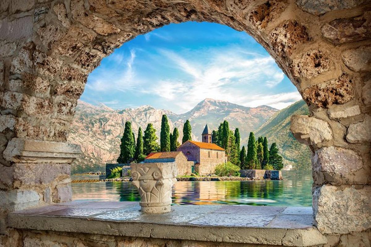 a view of a church from a stone archway with a lake and mountains