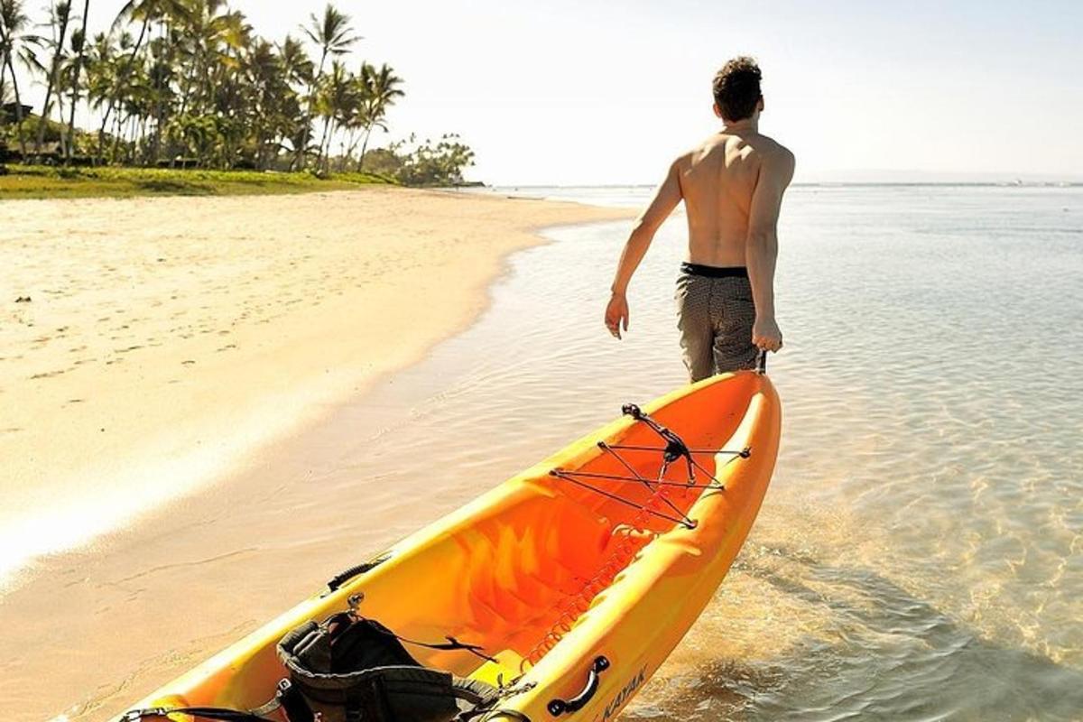 Un hombre parado en la playa junto a un kayak naranja.