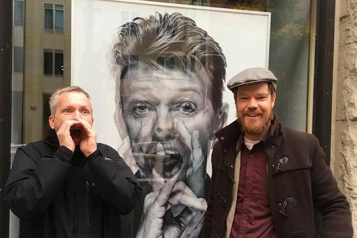 two men are standing in front of a painting of a man