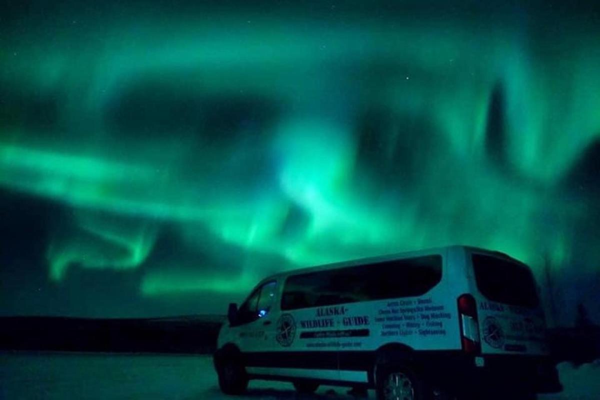 Una camioneta blanca estacionada frente a la aurora boreal