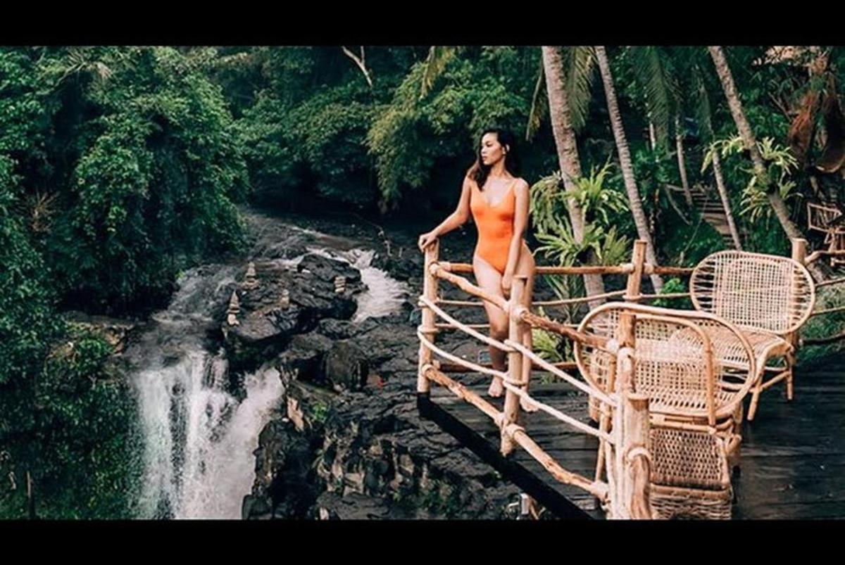 Kona í bikiní stendur á brú yfir foss