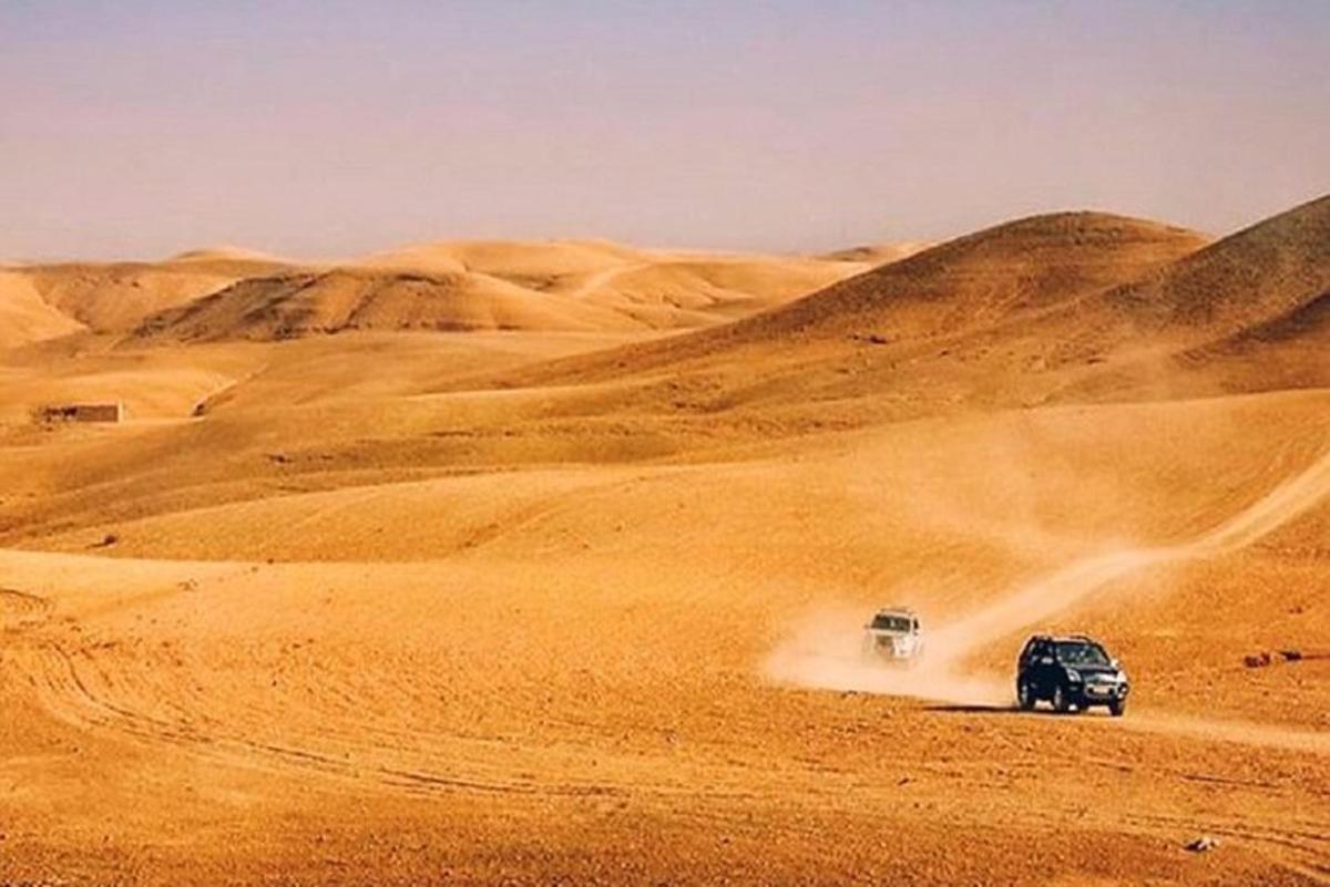 Un camión que circula por el desierto con dos coches.