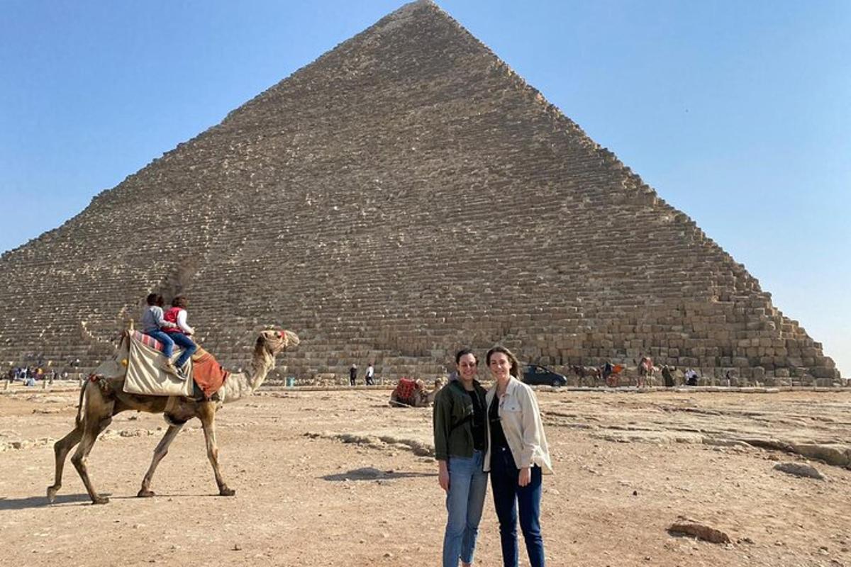 skupina lidí stojící vedle velblouda před pyramidou