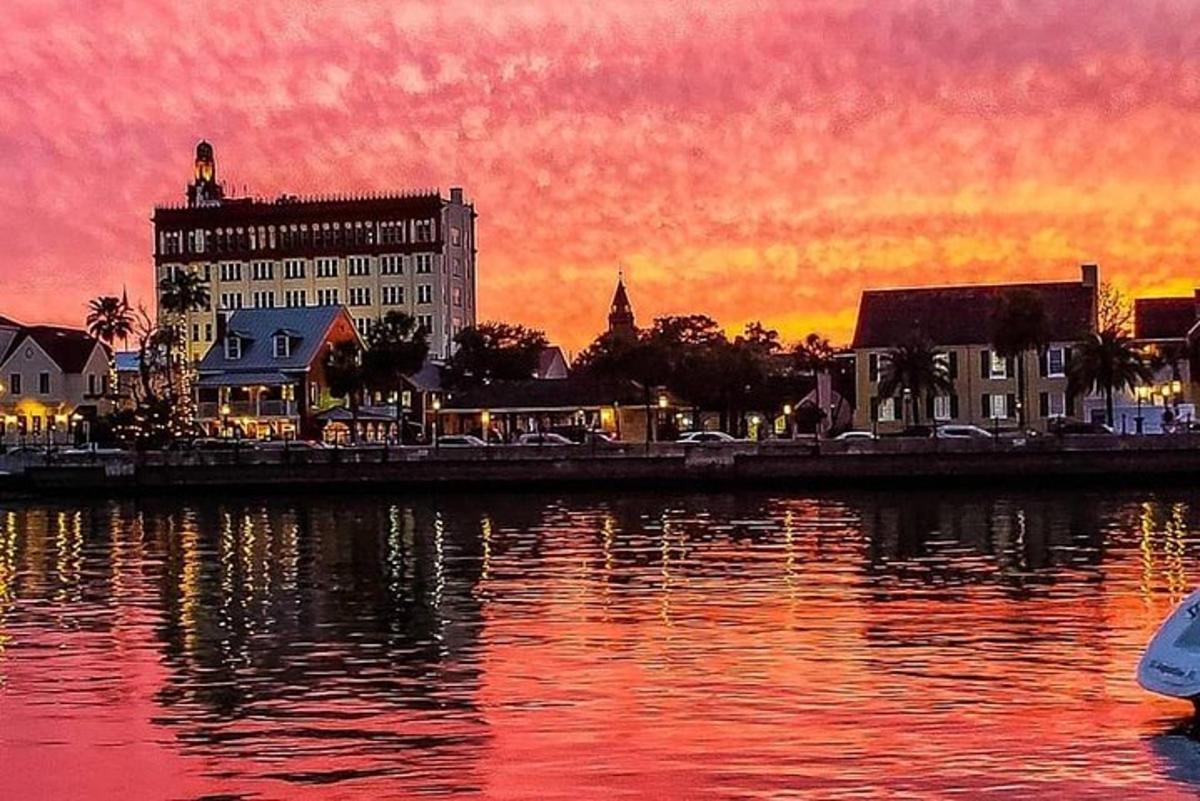 una posta de sol sobre una ciutat amb un edifici i l'aigua