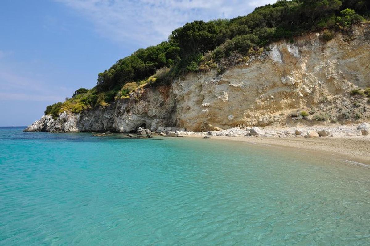 a beach with blue water and a rocky cliff