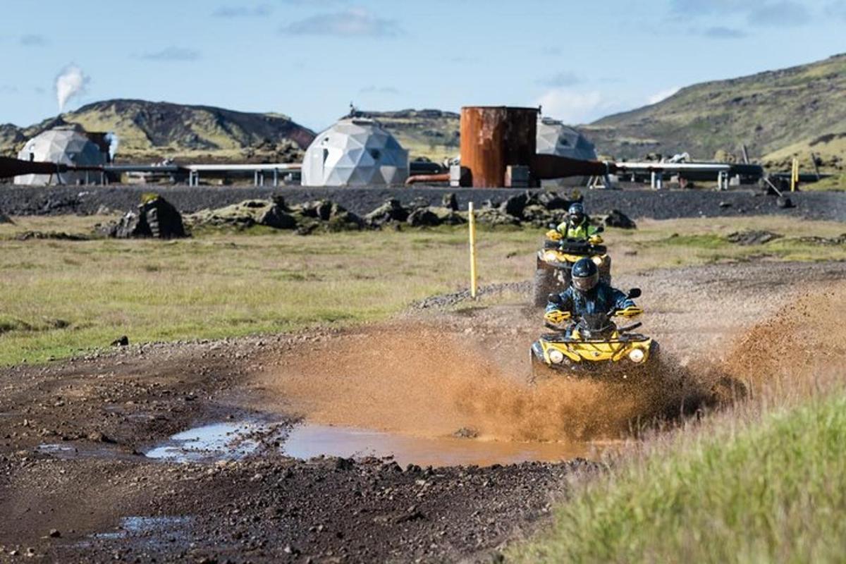 Dos personas viajando en un vehículo de cuatro ruedas a través de un charco de barro