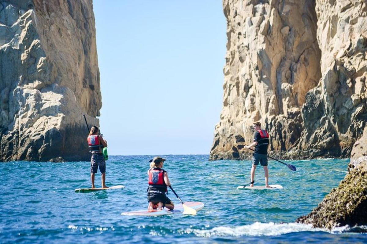 Tres personas en tablas de paddle surf en el agua cerca de un acantilado