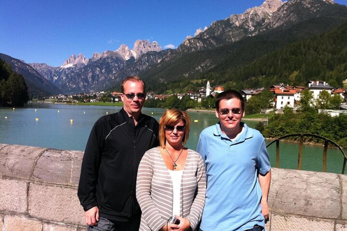 Tres personas de pie en una pared con un lago y montañas.