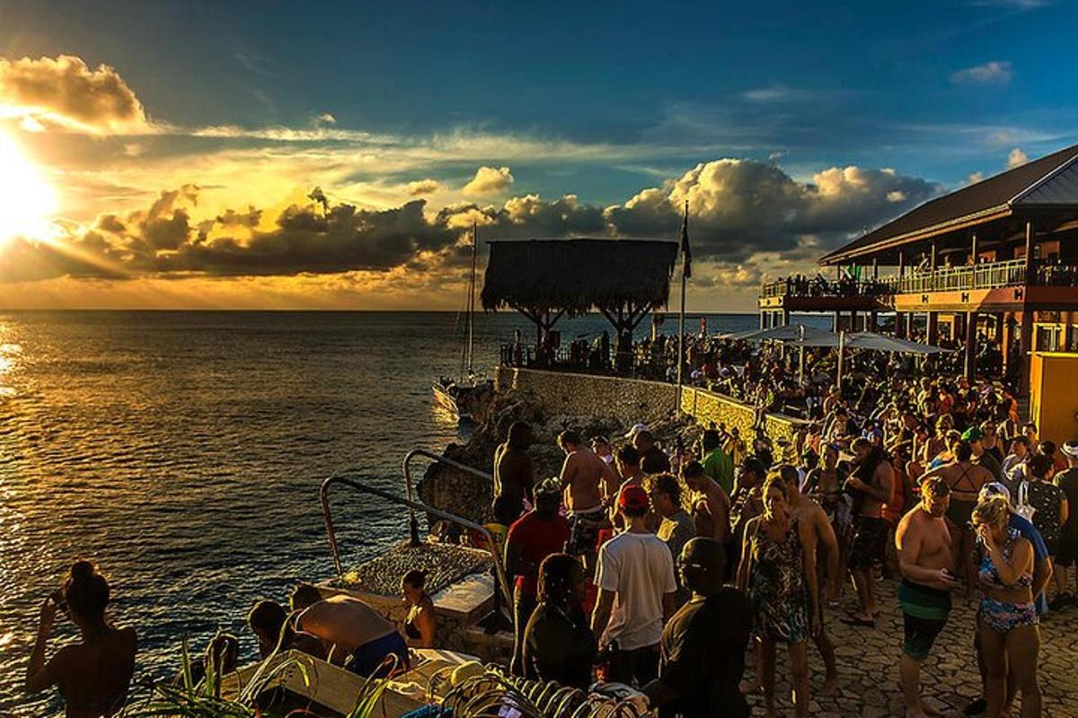 una folla di persone in piedi sulla spiaggia a guardare il tramonto