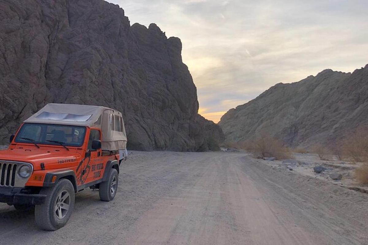 an orange jeep driving down a dirt road in a canyon