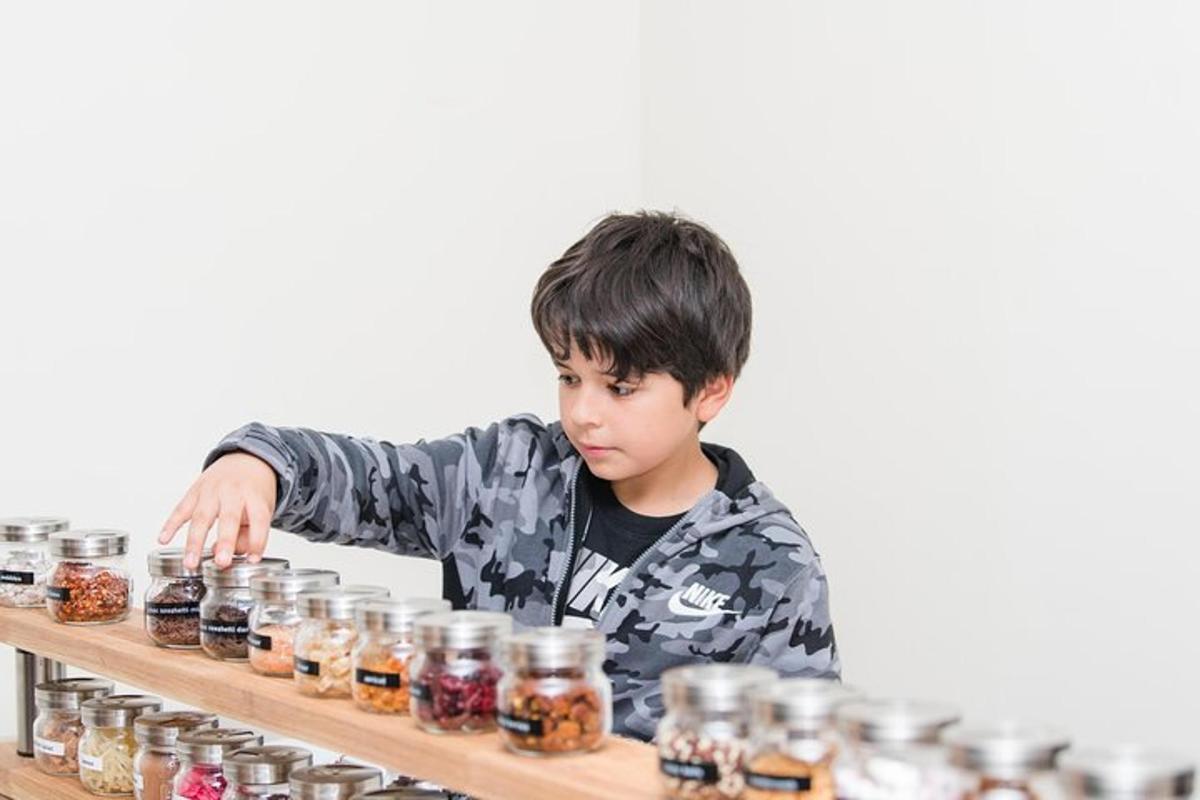 a young boy in a camo jacket standing behind a shelf of jars