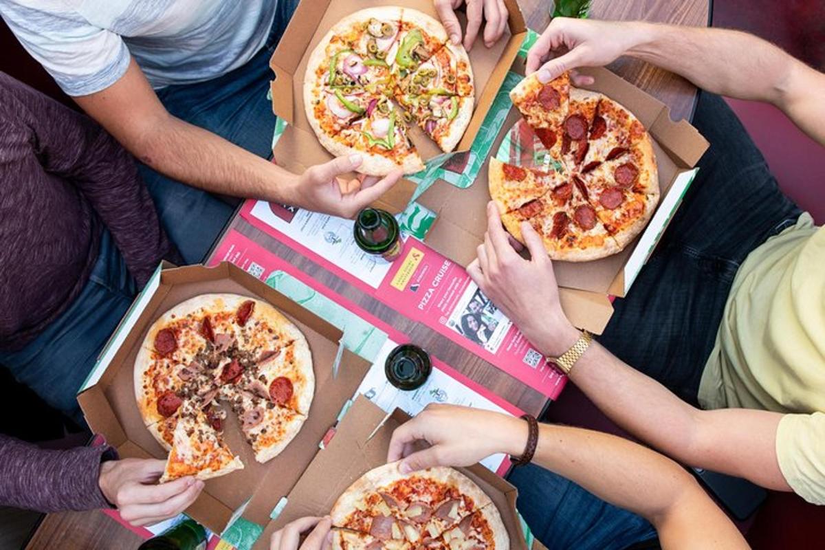 skupina lidí sedících kolem stolu s pizzami