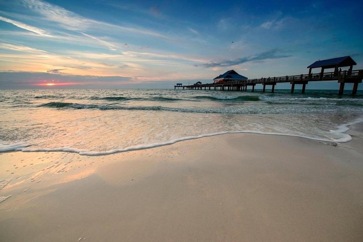 a beach with a pier in the ocean at sunset