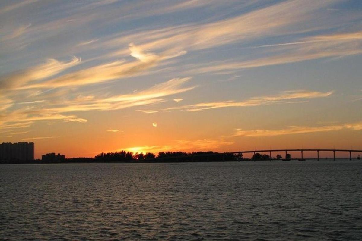 a sunset over the water with a bridge in the background