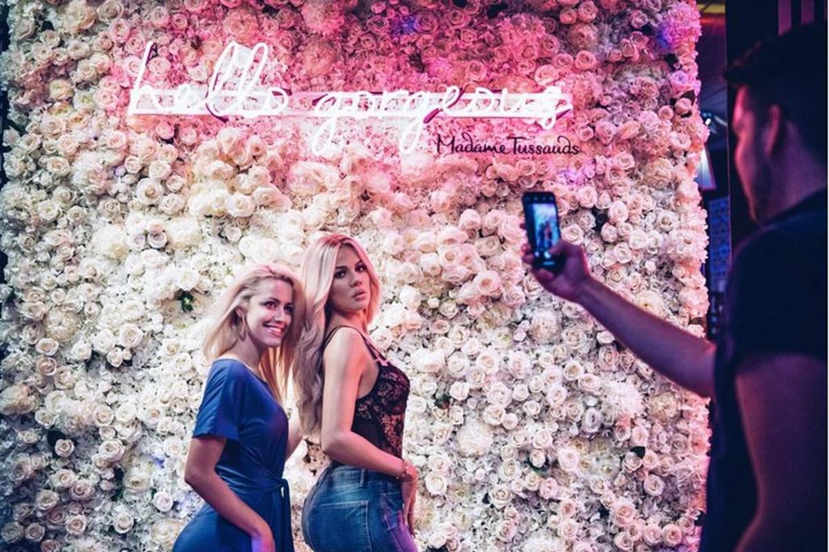 two women standing in front of a wall of flowers