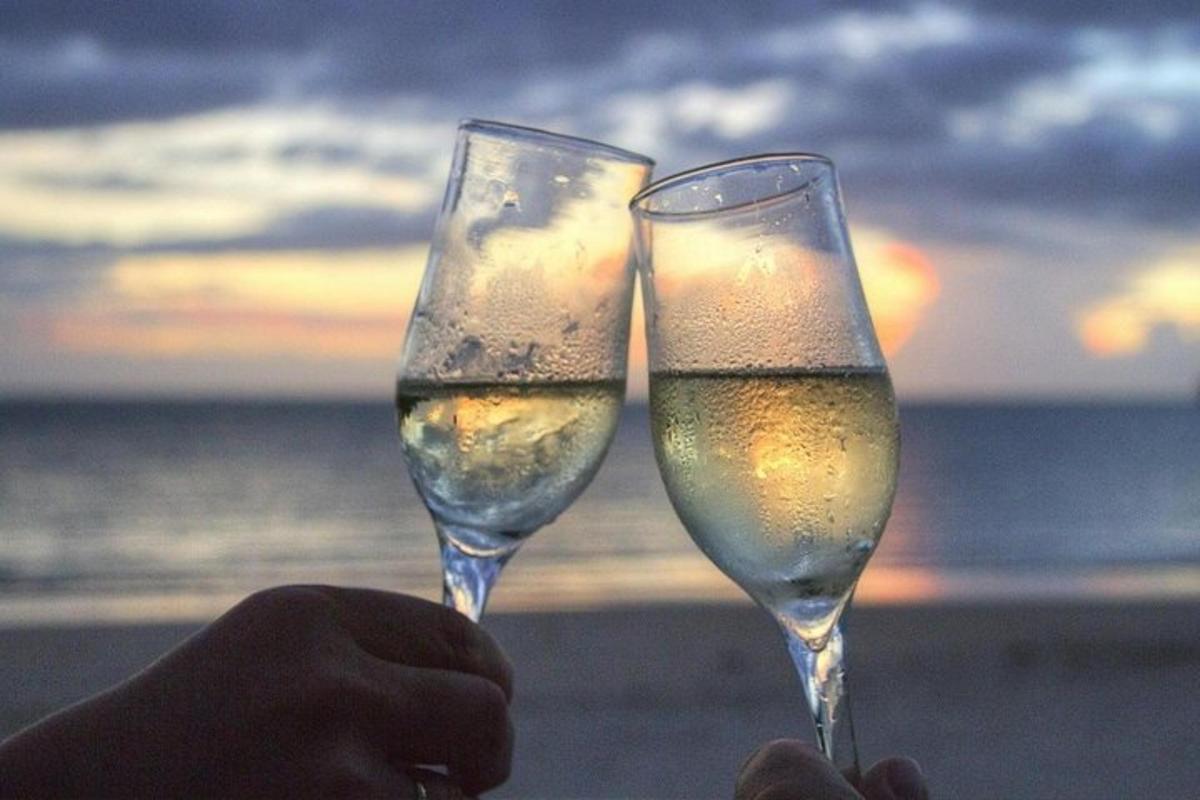 two people holding champagne glasses in front of the ocean