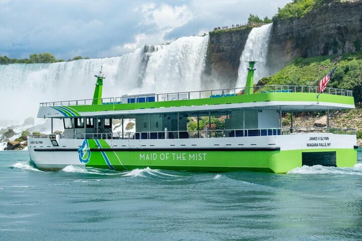 a green and white boat in front of a waterfall