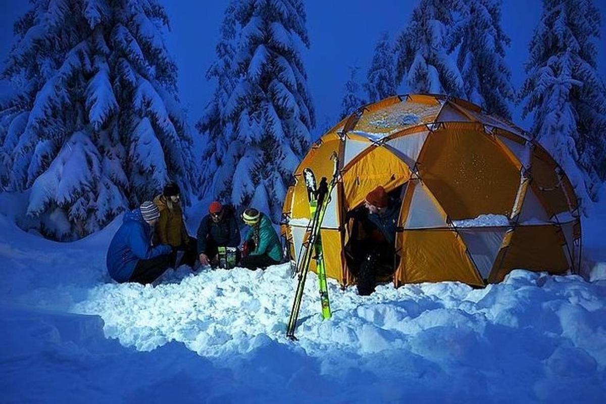 um grupo de pessoas sentadas na neve ao lado de uma barraca
