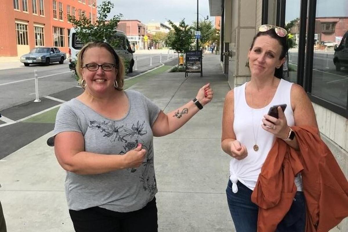 two women standing on a sidewalk with a cell phone