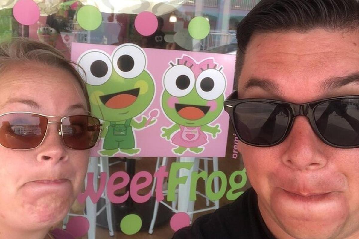 um homem e uma mulher usando óculos escuros em frente a uma placa estranha de sapo