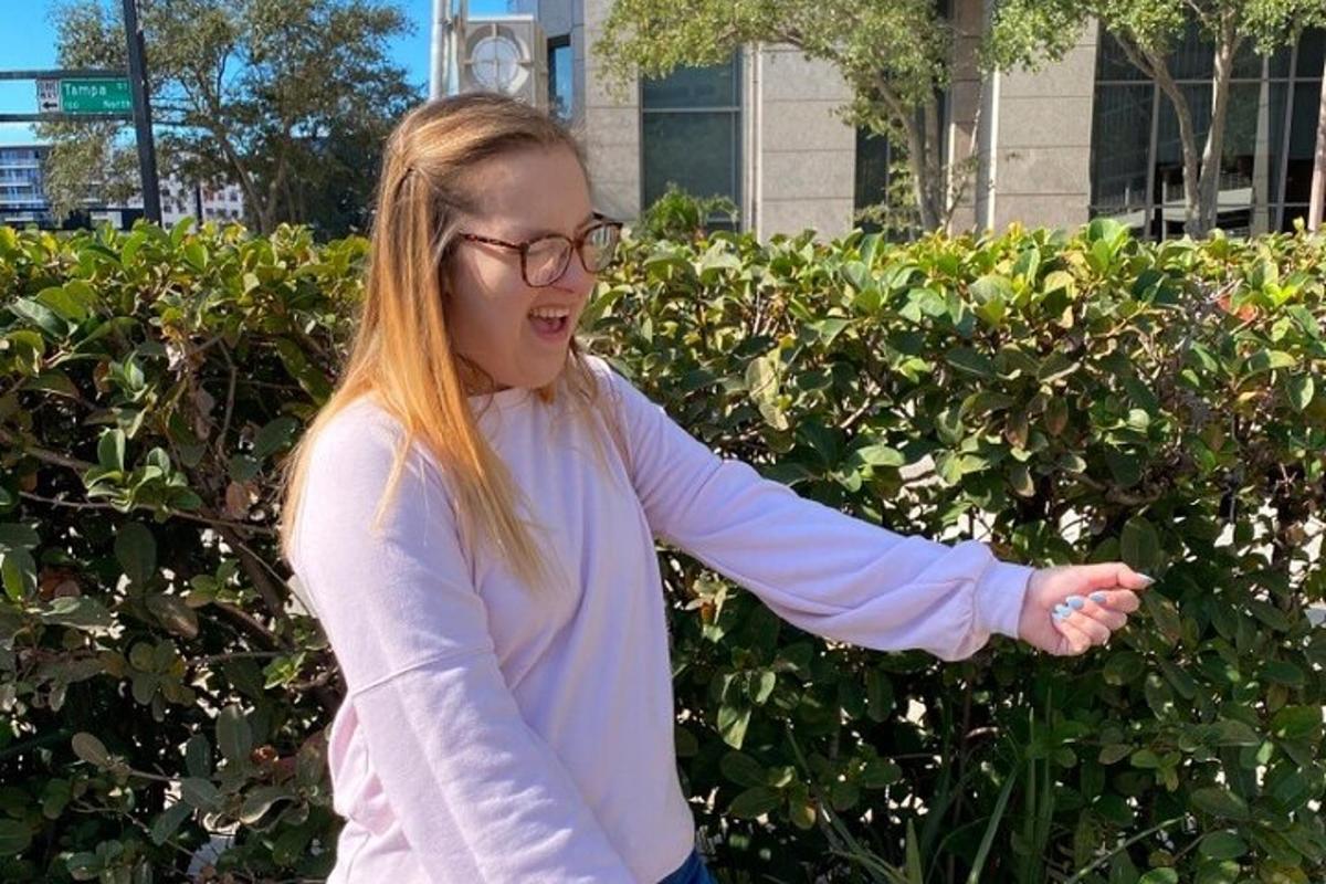 a woman in glasses is standing in front of a hedge