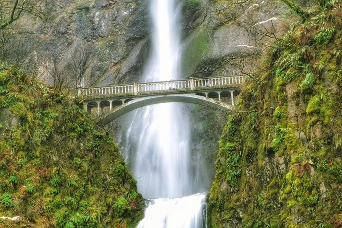 a bridge over a waterfall in front of a mountain
