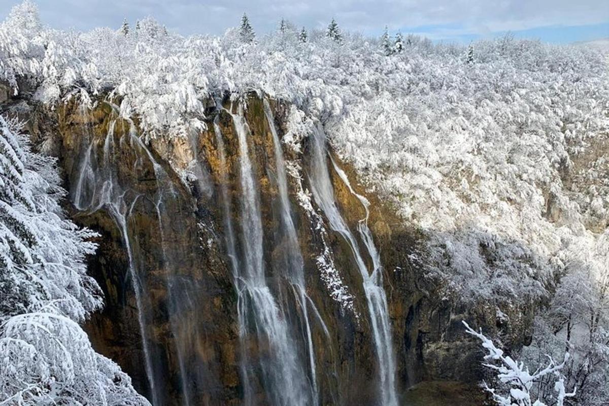 a waterfall with snow covered trees on top of it