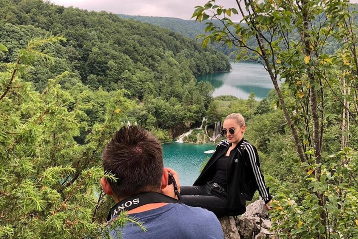 a man taking a picture of a man sitting on a rock near a lake