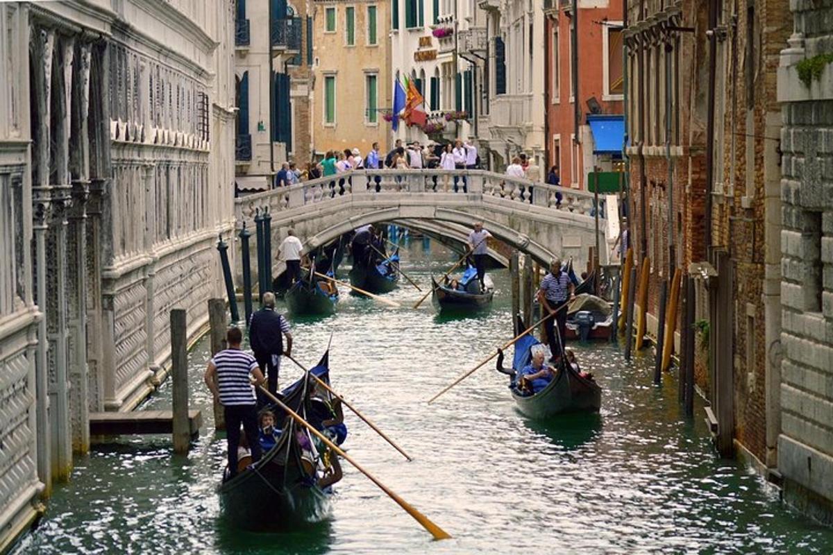 a group of gondolas in a canal with people on a bridge