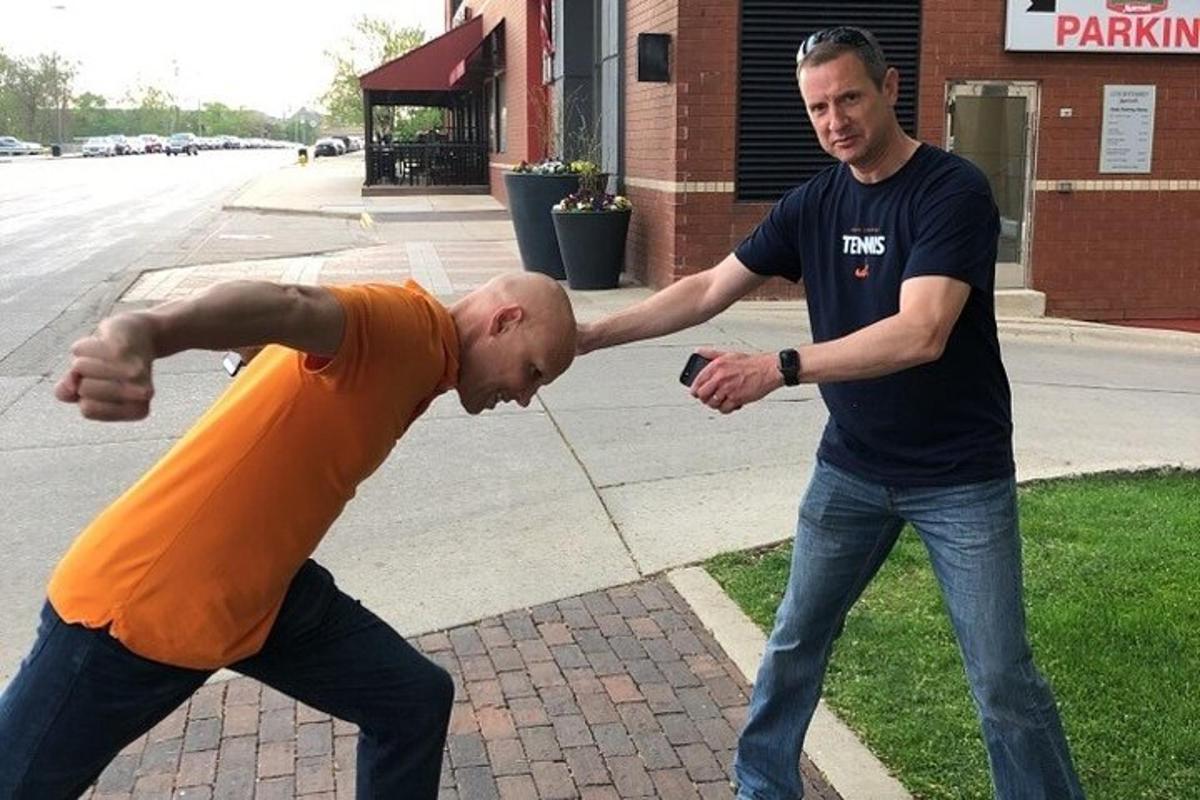 two men standing on a sidewalk looking at a cell phone