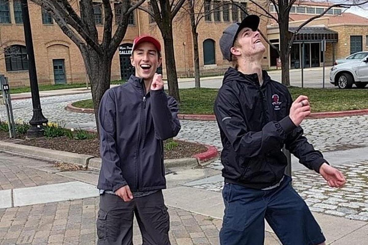 dva mladí muži stojící na chodníku a telefonující po mobilu