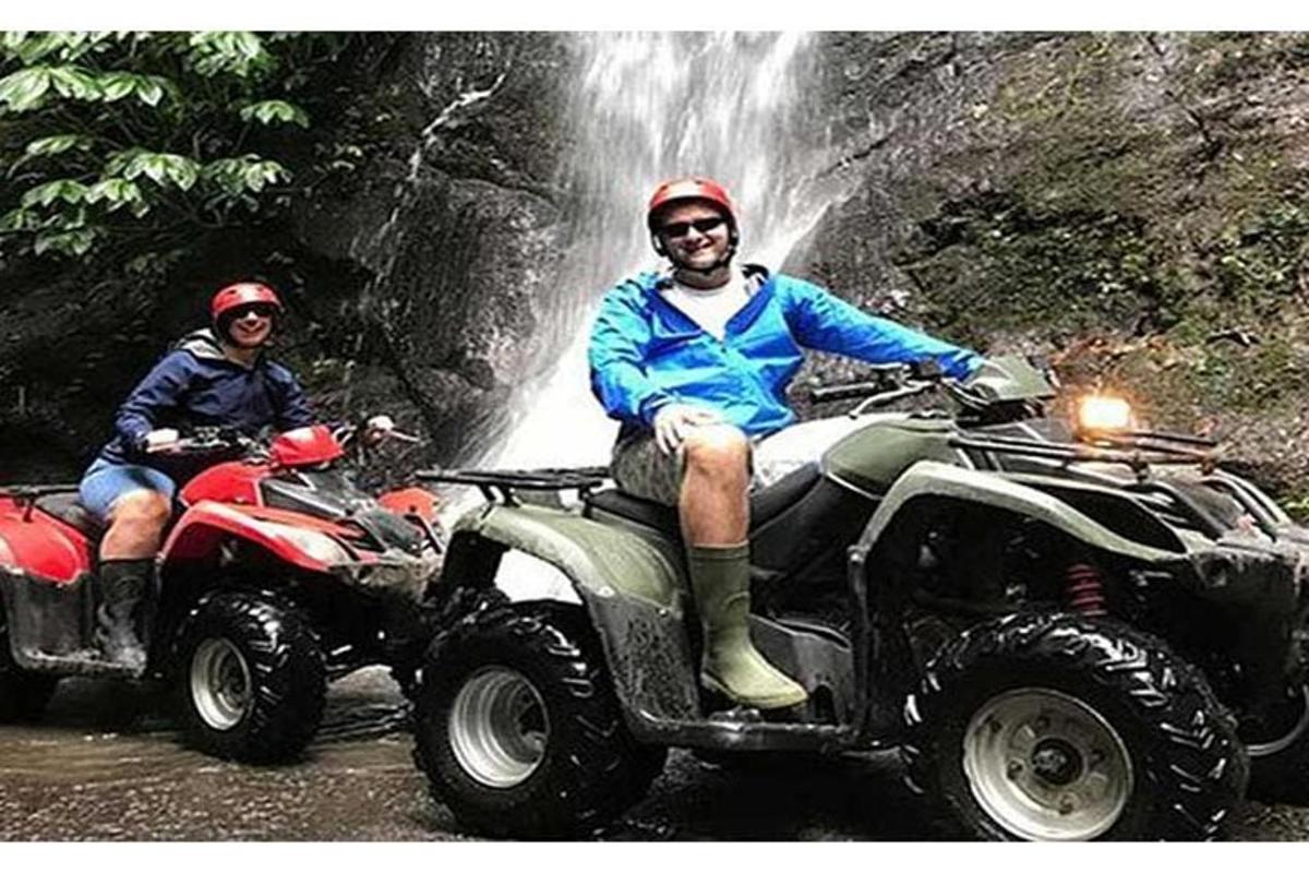 two people riding atvs in front of a waterfall