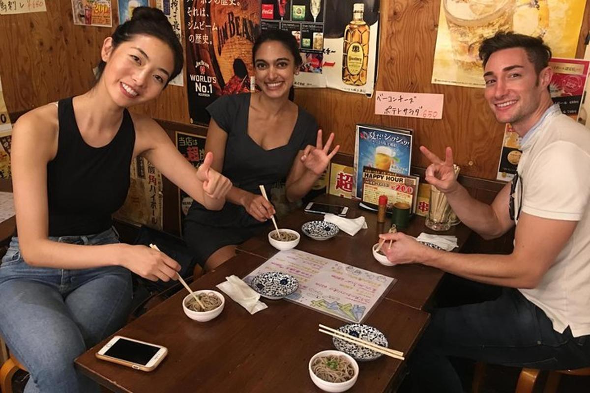 a group of people sitting around a table eating noodles