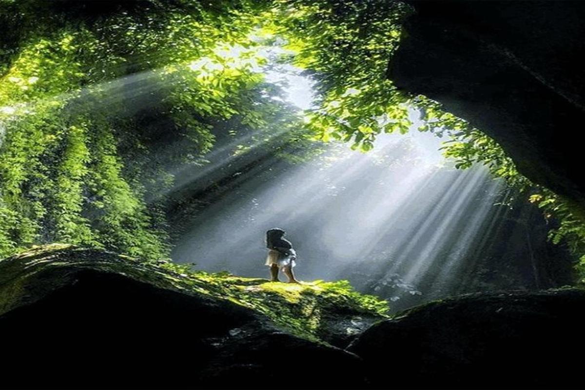 uma pessoa parada no meio de uma caverna com o sol brilhando