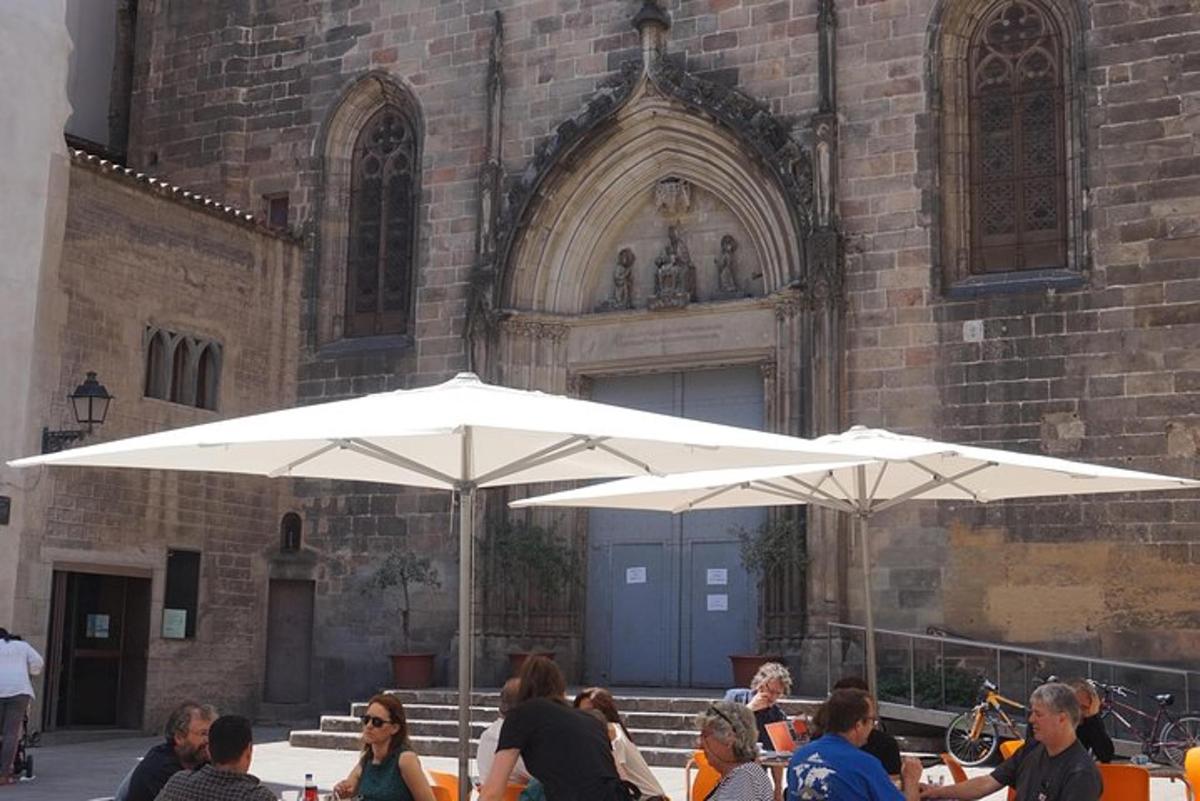 gent asseguda a taules sota para-sols blancs davant d'un edifici