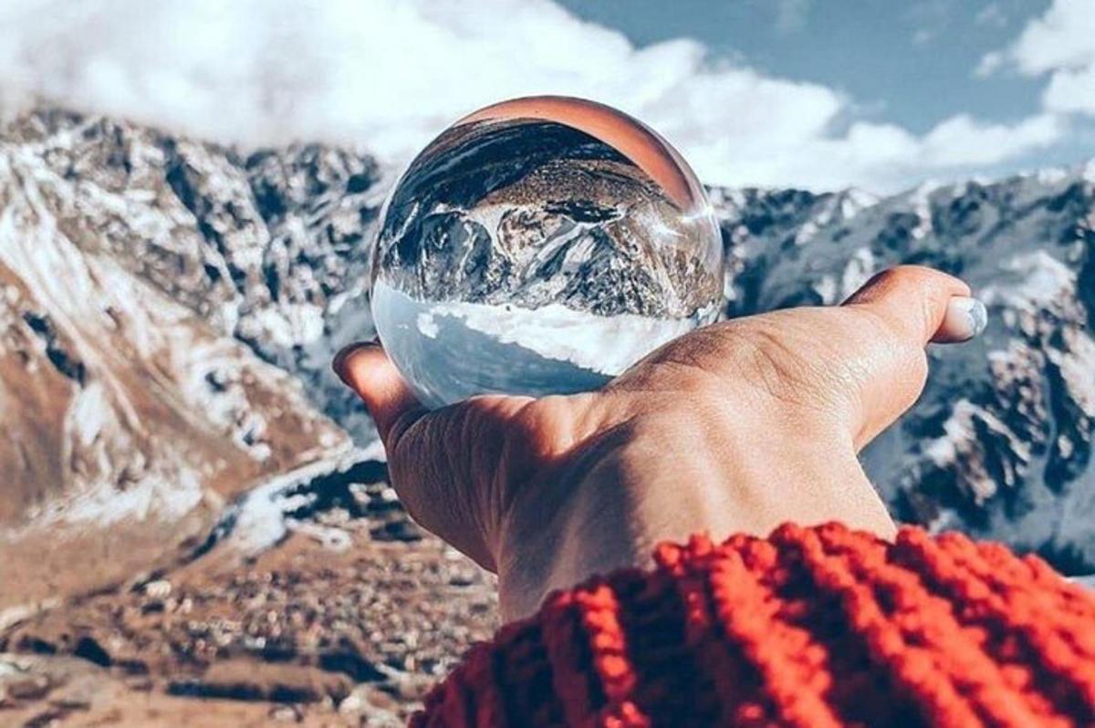 a hand holding a glass ball in front of a mountain