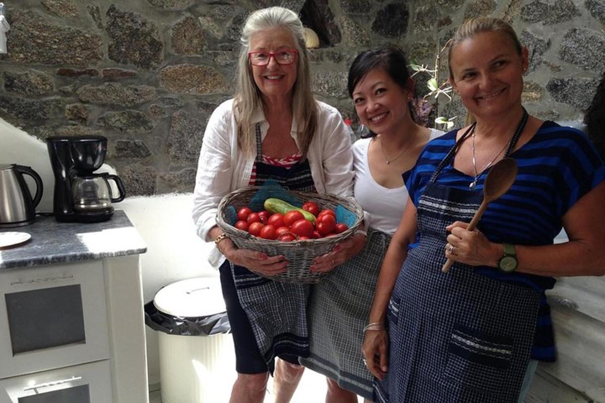 três mulheres em pé na cozinha segurando uma cesta de tomates