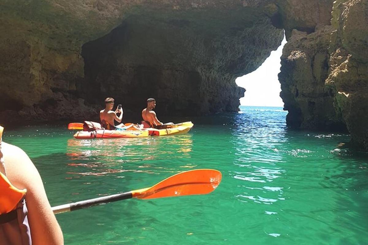 three people kayaking in the water near a cave