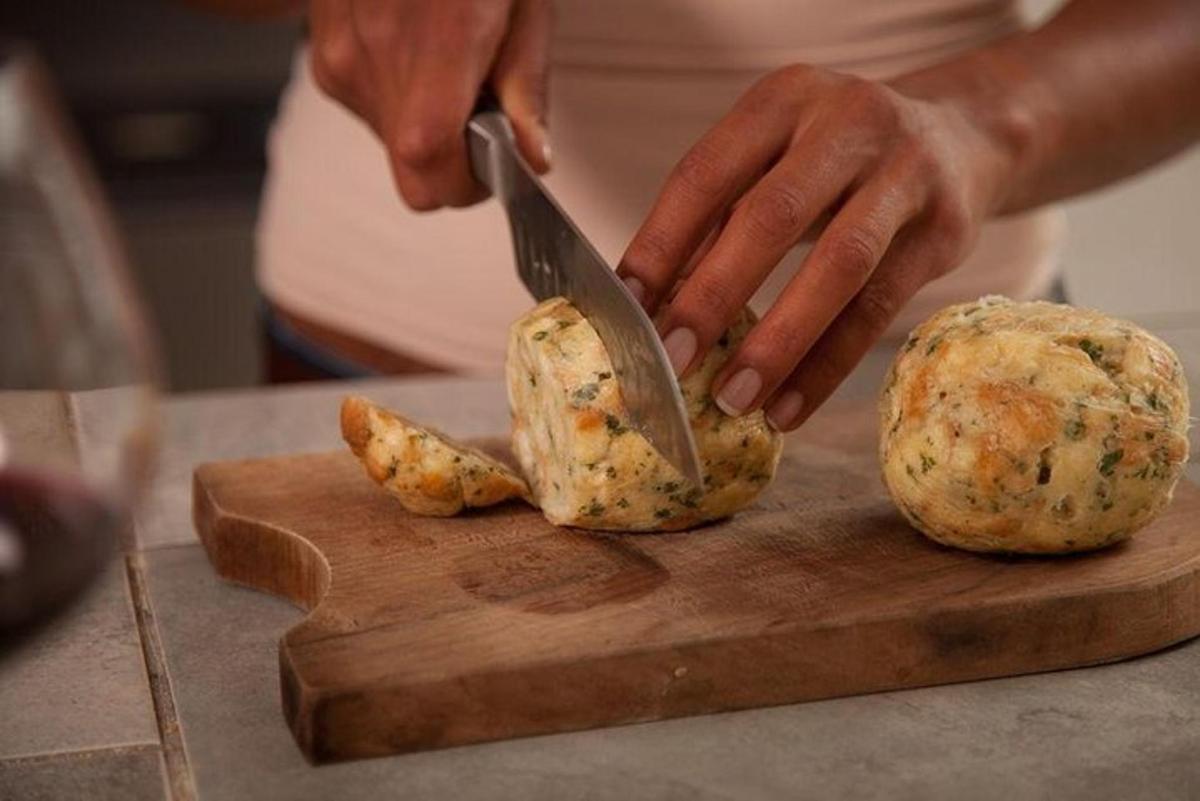 een vrouw die aardappelen snijdt op een snijplank met een mes