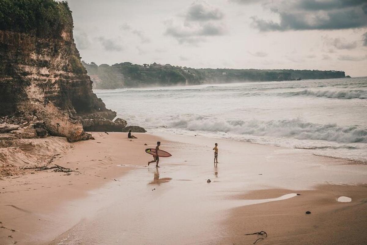 skupina ljudi, ki se sprehajajo po plaži z desko za surfanje