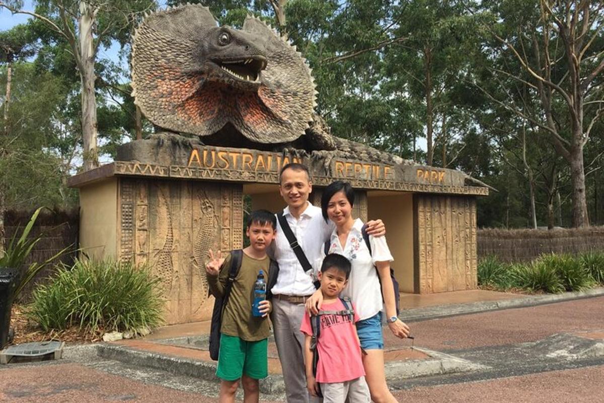 seorang lelaki dan dua kanak-kanak berdiri di hadapan monumen dinosaur