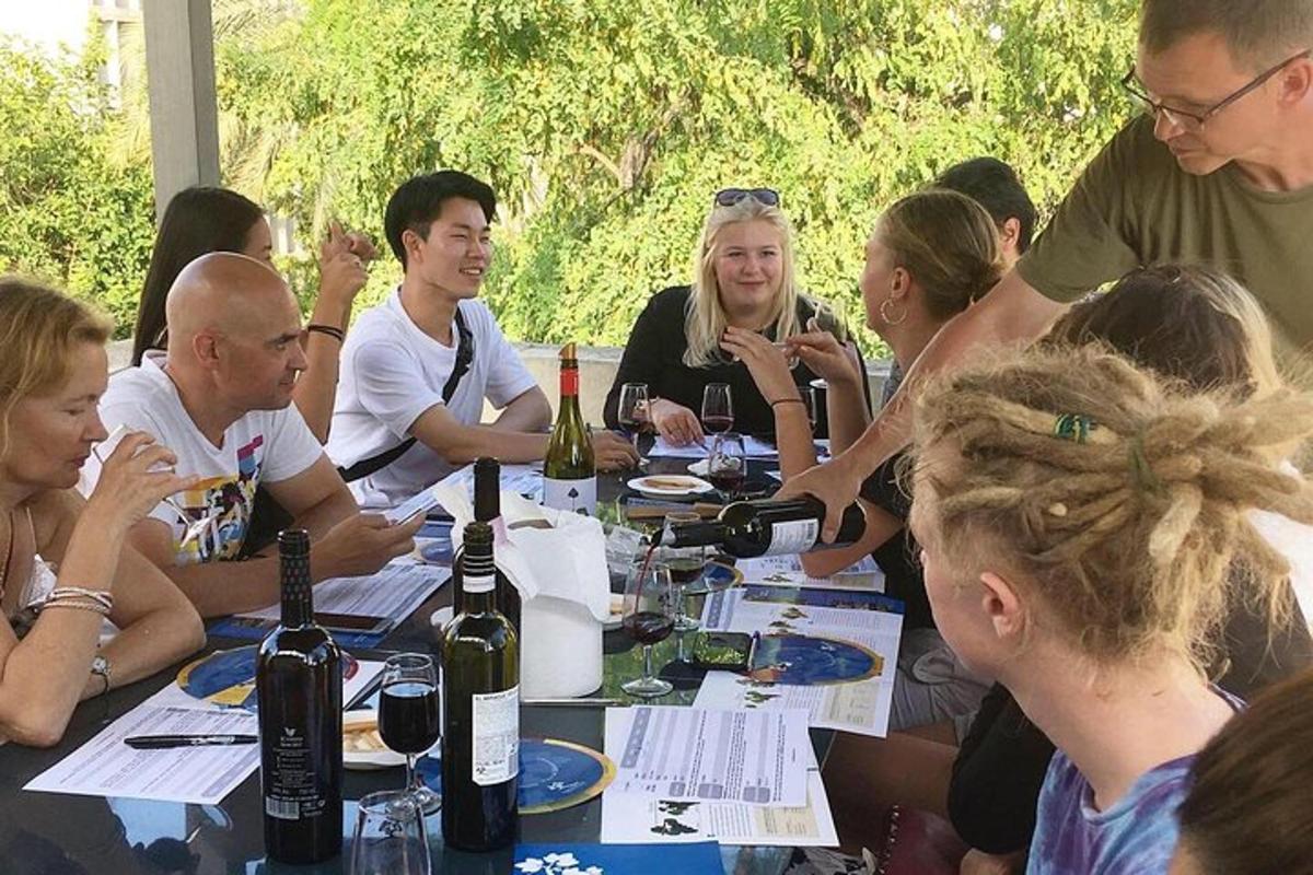 skupina lidí sedících kolem stolu s lahvemi vína