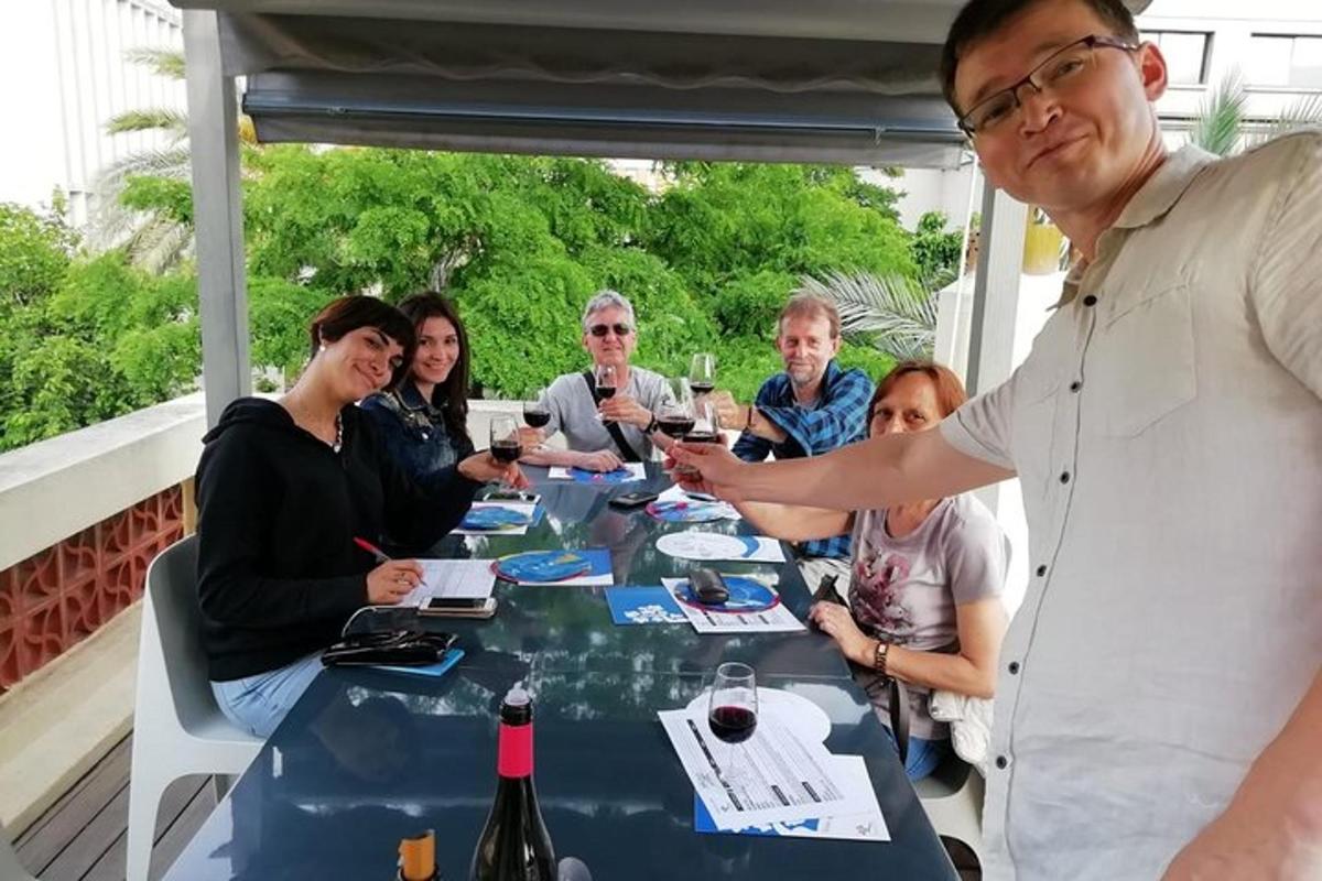 skupina lidí sedících kolem stolu s lahvemi vína