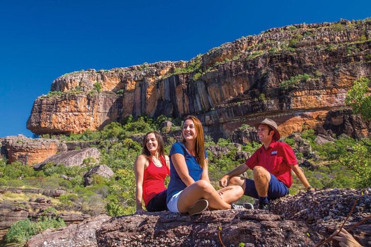 three people sitting on a rock in front of a mountain