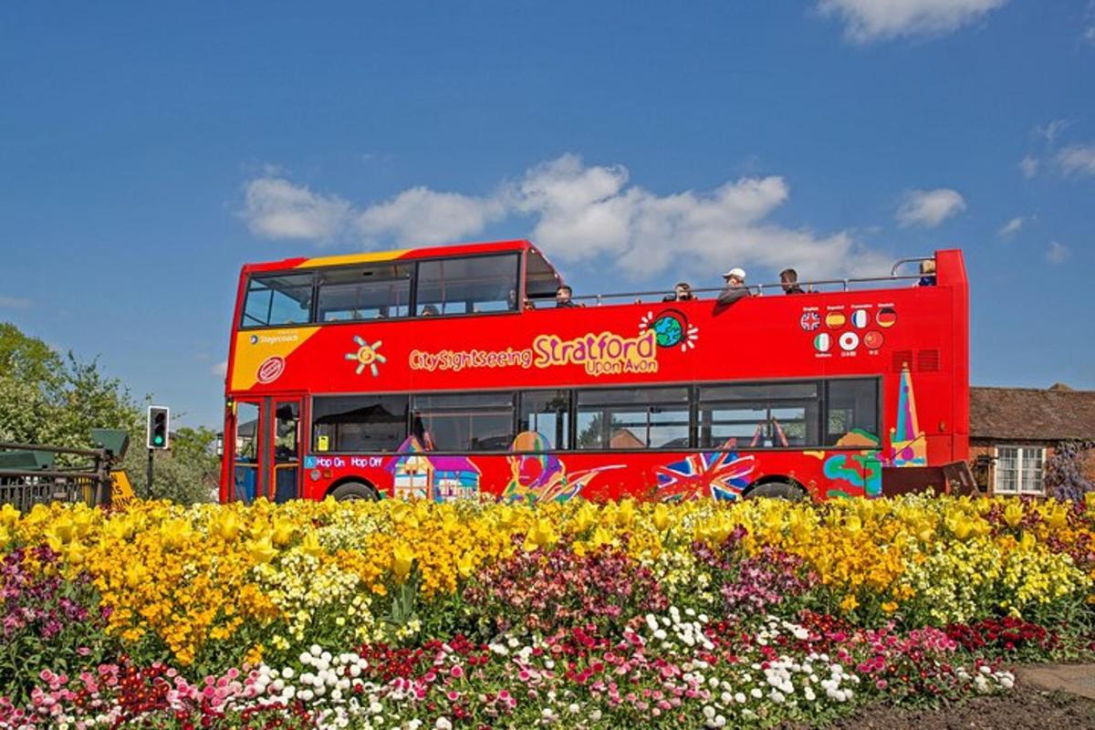a red double decker bus driving past a garden of flowers