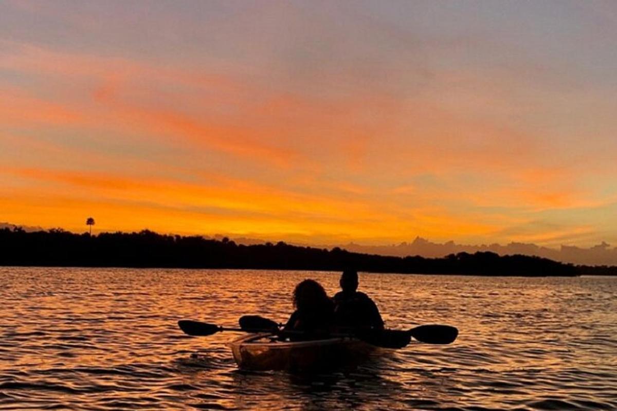 two people sitting in a boat on the water at sunset
