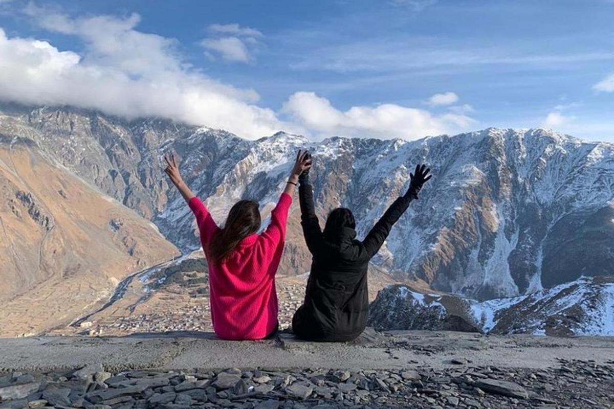 two people sitting on top of a mountain with their hands up