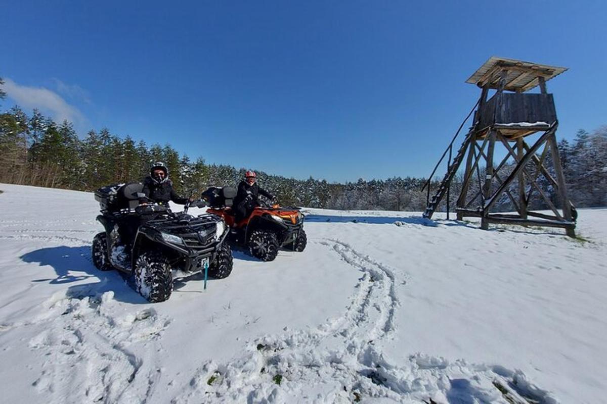 two people on atvs in the snow next to a tower