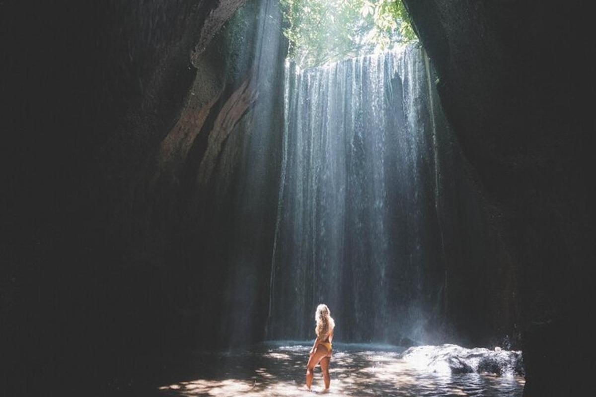a woman standing in the water in front of a waterfall