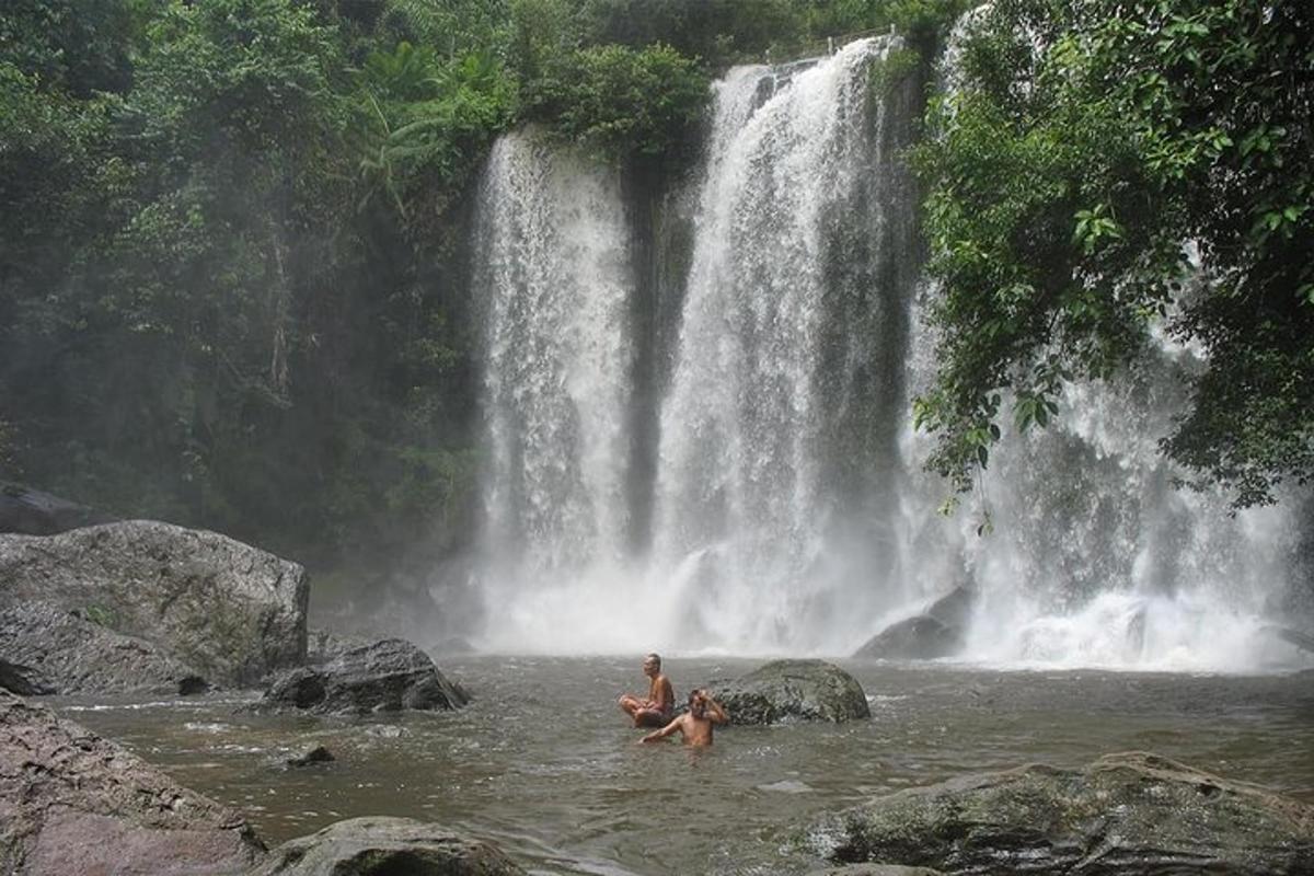 deux personnes assises dans l'eau devant une cascade